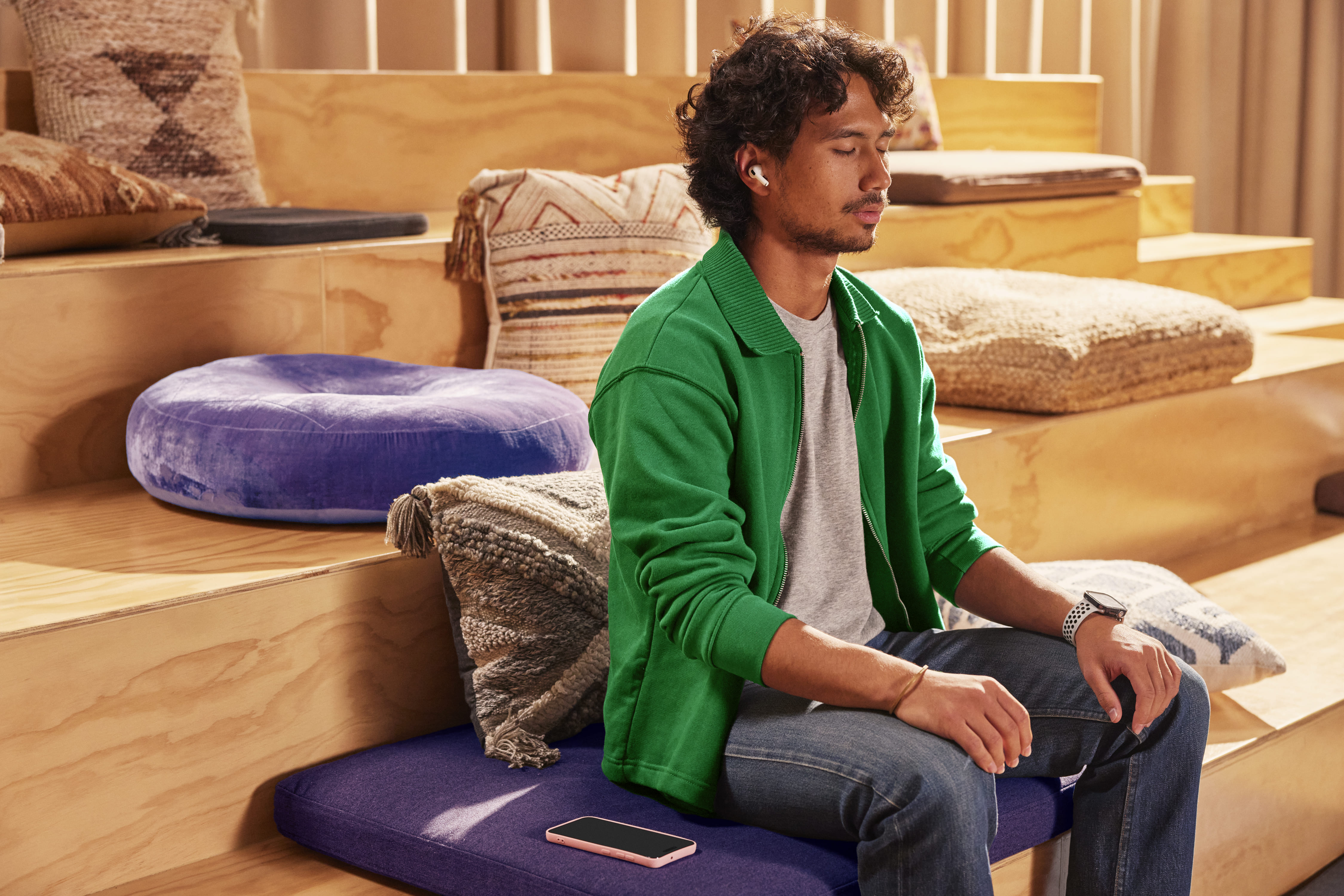 Young man wearing earbuds relaxes on a sofa beside a laptop in a warmly lit home.