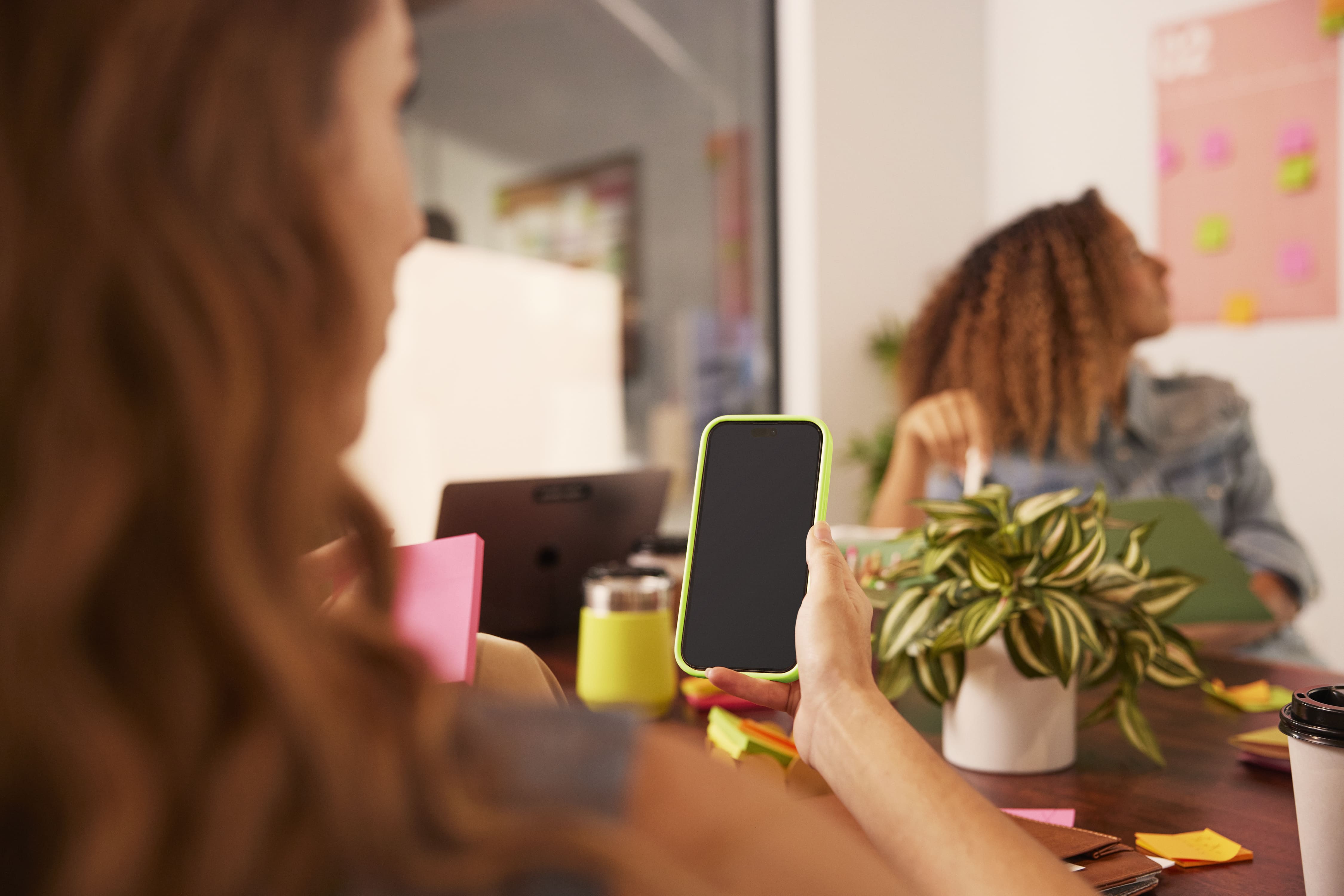 Blurred business professionals collaborate around a smartphone in a colorful modern office workspace.