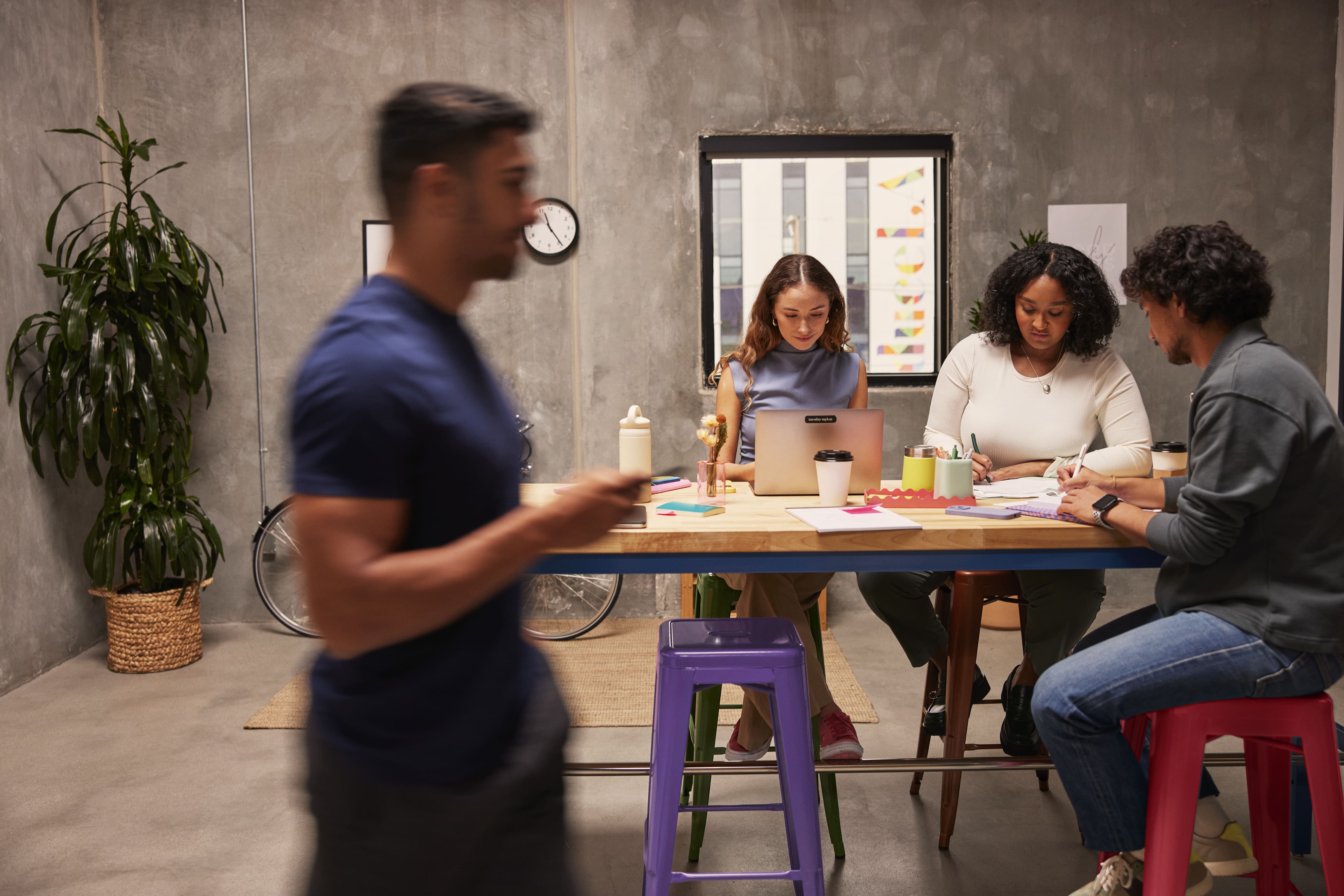 Diverse coworkers collaborate around a meeting table in a modern, plant-filled office.