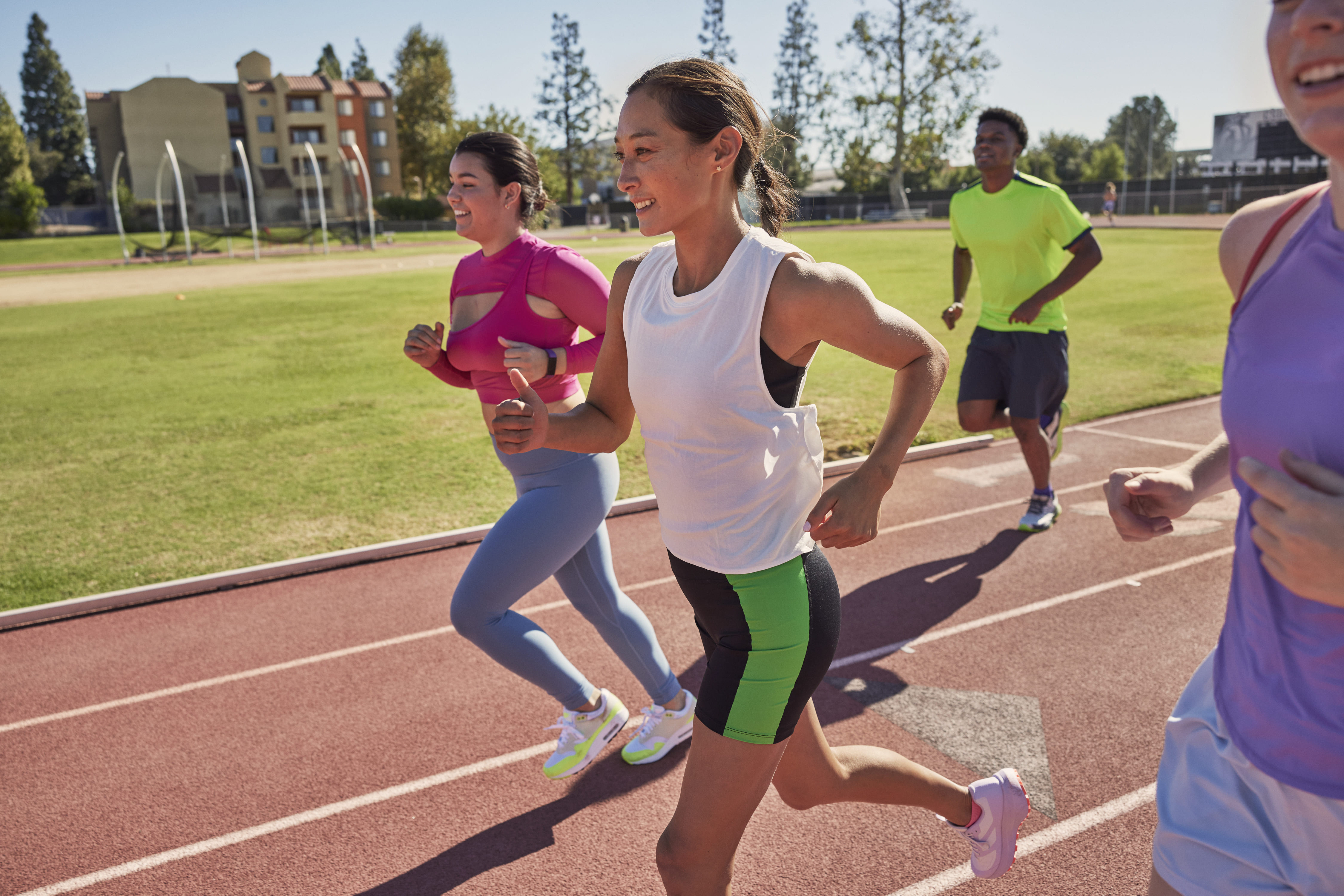 A diverse group of women jogs together on an outdoor track in bright afternoon sunlight.