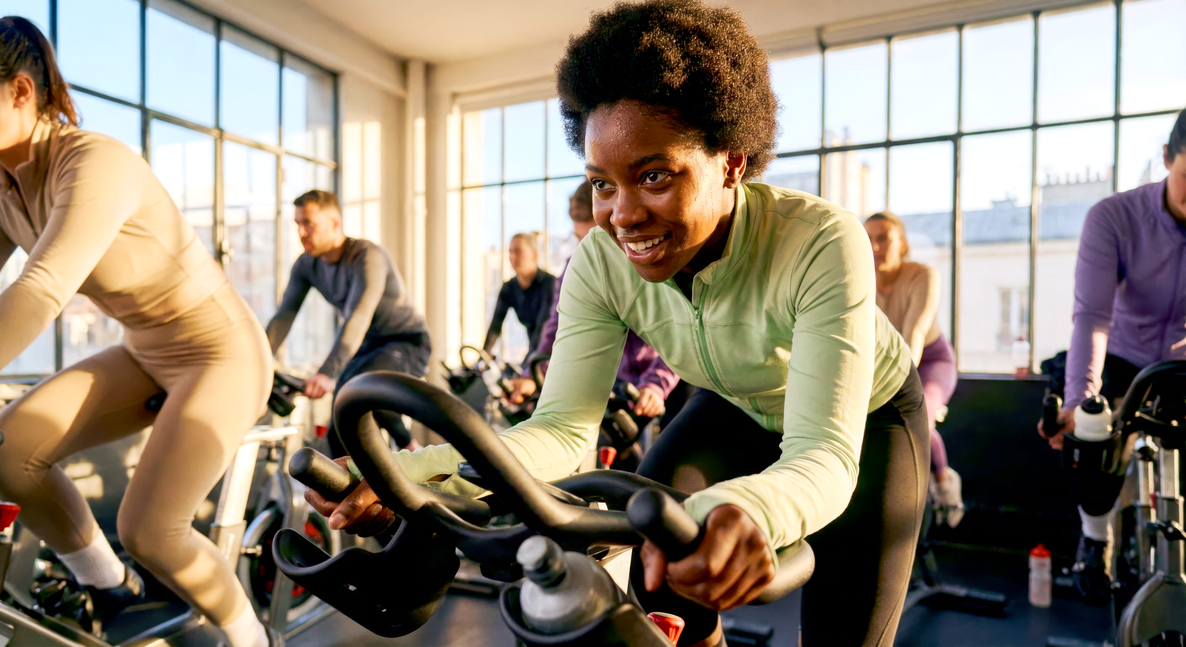 Energetic indoor cycling class participants pedal together in a bright studio filled with natural light.