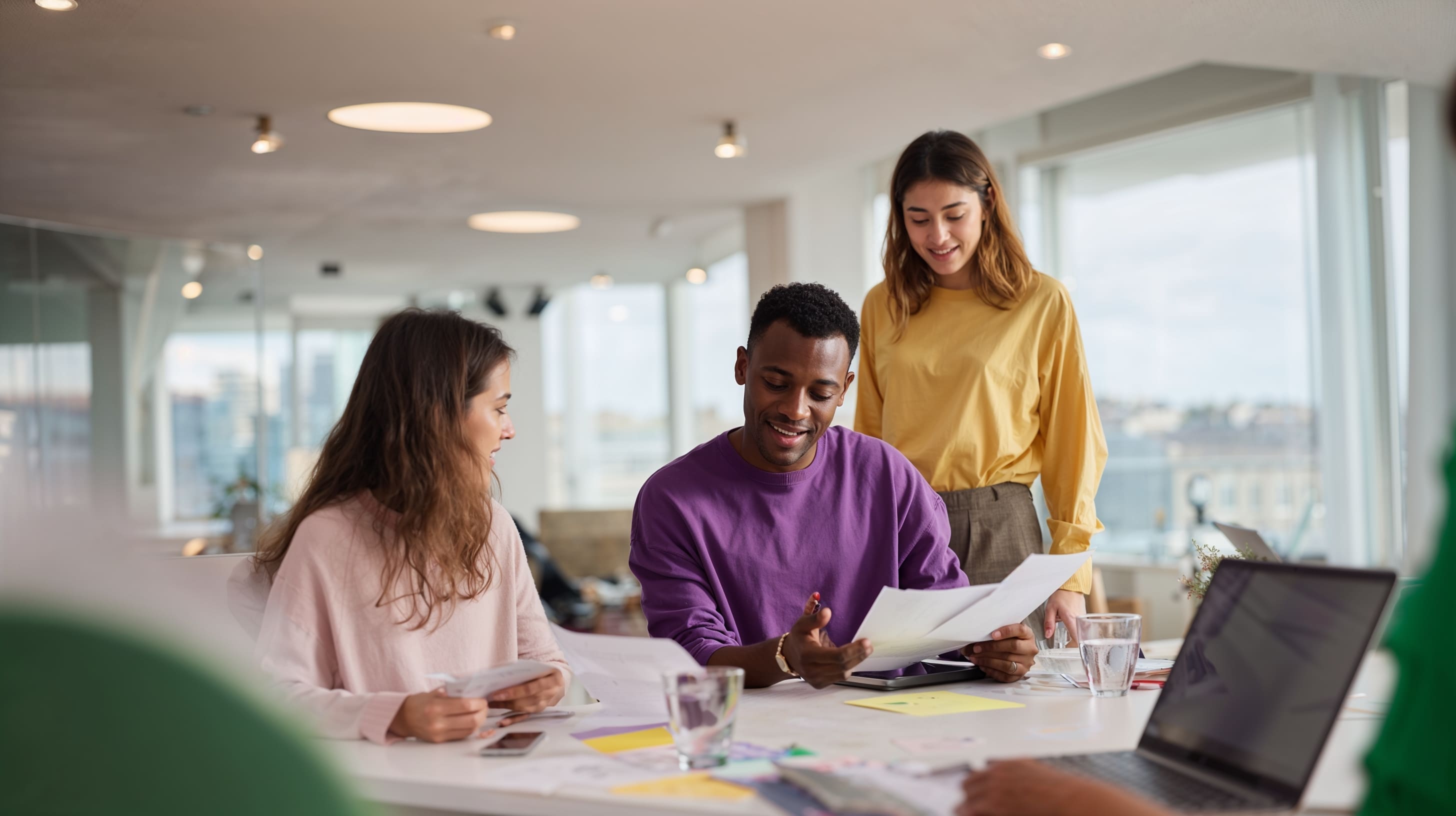 Diverse colleagues collaborate around a table reviewing documents in a bright modern office