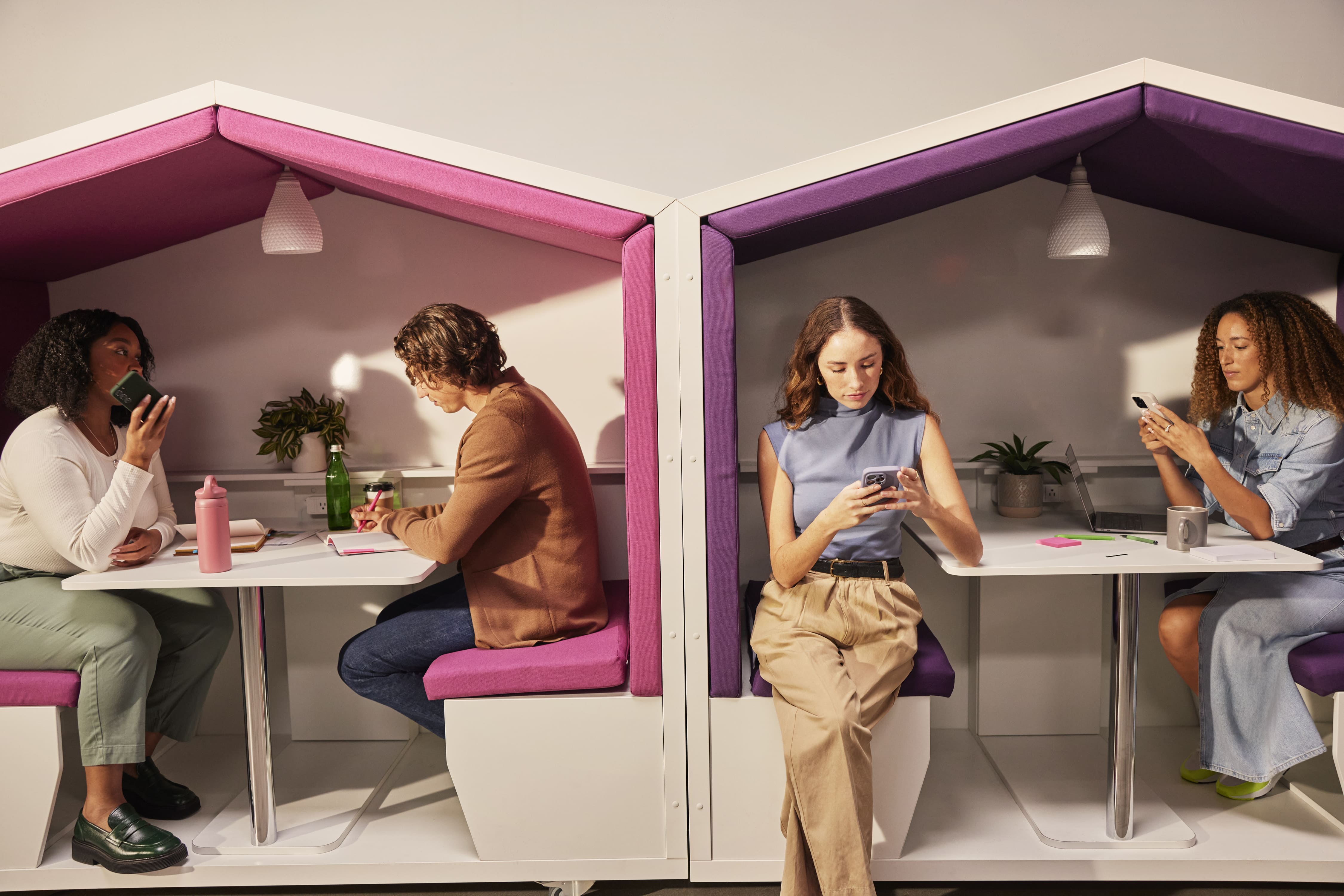 Diverse coworkers collaborate at shared desks in a colorful modern office with purple acoustic panels.